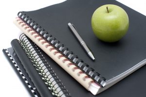 Spiral bound notebooks for taking university notes topped with a pen and fresh healthy green apple to eat as a snack while studying